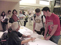 photograph of Ronald Takaki, sitting at table and signing books while chatting with students