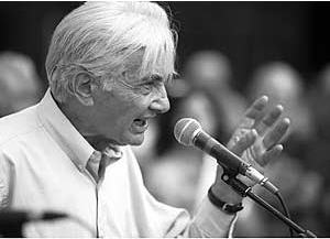 a black and white photograph of Howard Zinn addressing the crowd